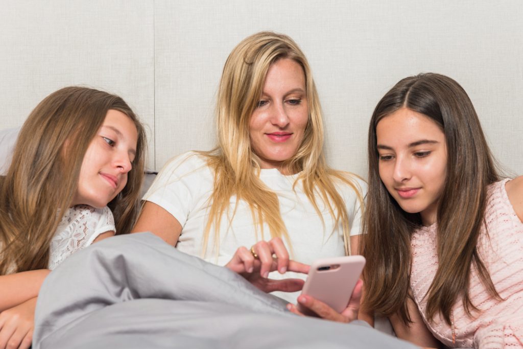 Madre con hijas adolescentes viendo un teléfono celular