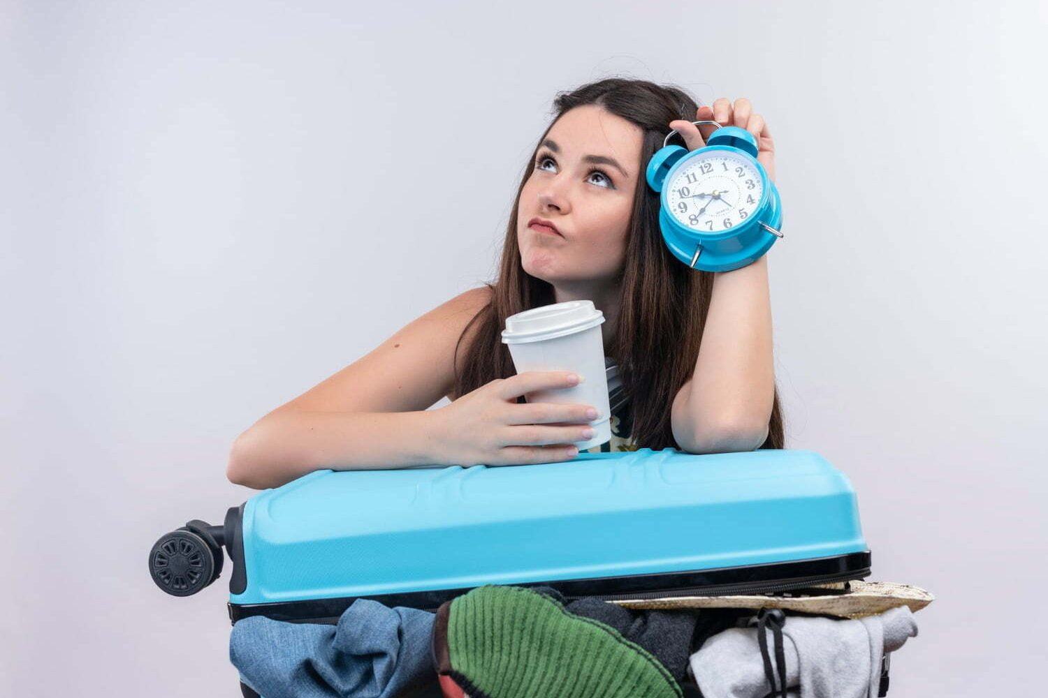 mujer con maleta abierta y desordenada sobre sus piernas, con un café y un despertador en sus manos, para volver a la rutina luego de vacaciones