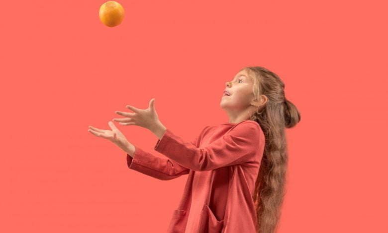 niña haciendo uso de sus reflejos, para atrapar una naranja en el aire.